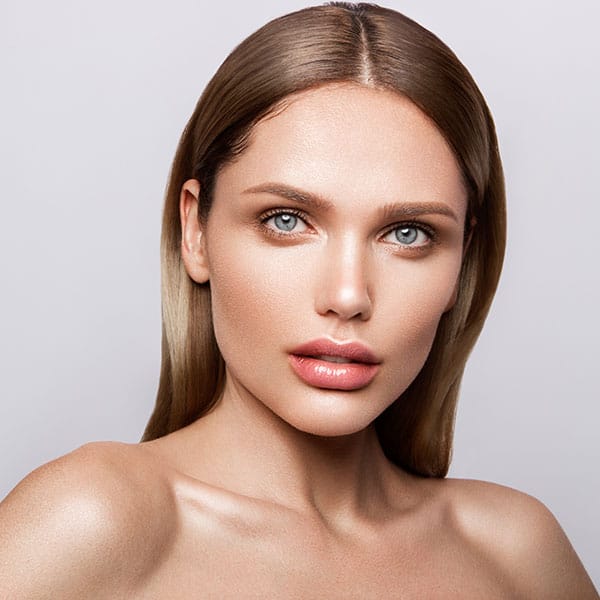 Stunning woman with clear skin and straight hair, showcasing beauty and confidence with a simple grey backdrop.